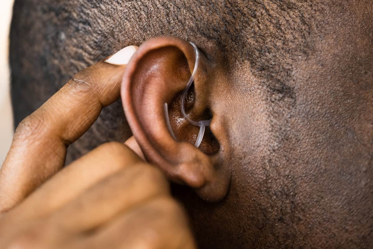 man touching hearing aid that is behind the ear