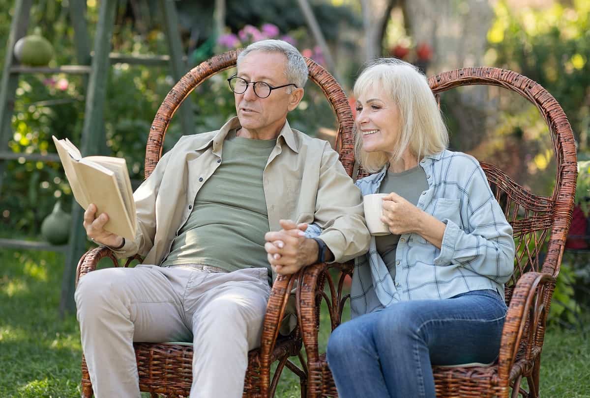 Elderly Couple Reading book together outside on wicker chairs